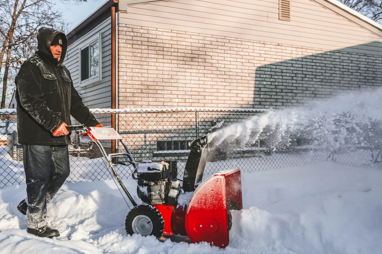 A man pushing a snow blower in his driveway